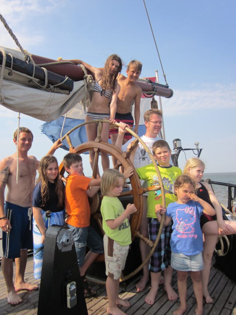 Kinder einer Segelgruppe sind ums Steuerrad versammelt