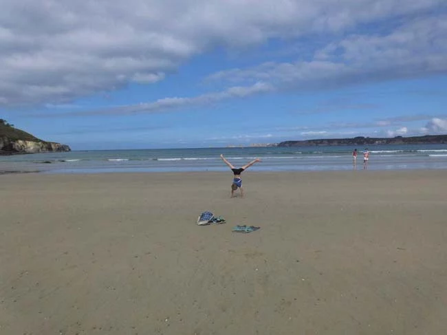 Am leeren Strand in der Bretagne macht ein Teenager einen Handstand.