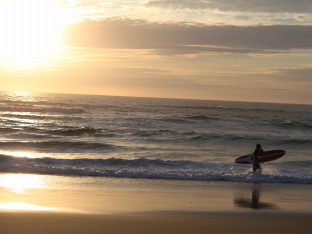 letzter Surfer verlässt bei Sonnenuntergang das Meer 