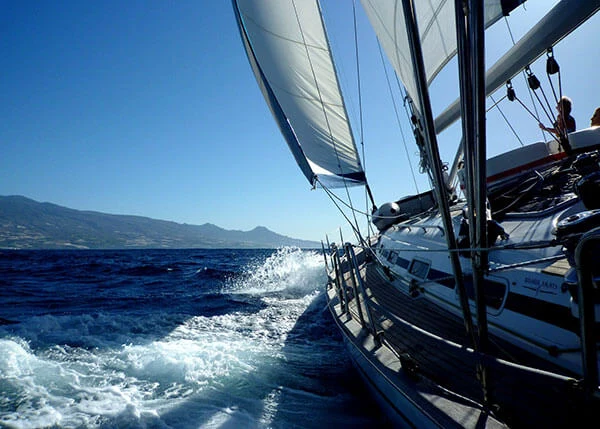 Blick auf Meer und Insel vom Deck der Yacht bei sportlichem Segeln