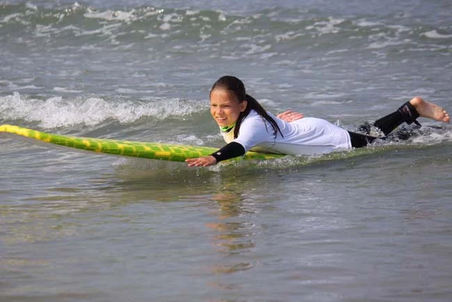 Mädchen paddelt auf dem Surfbrett liegend durch den Atlantik