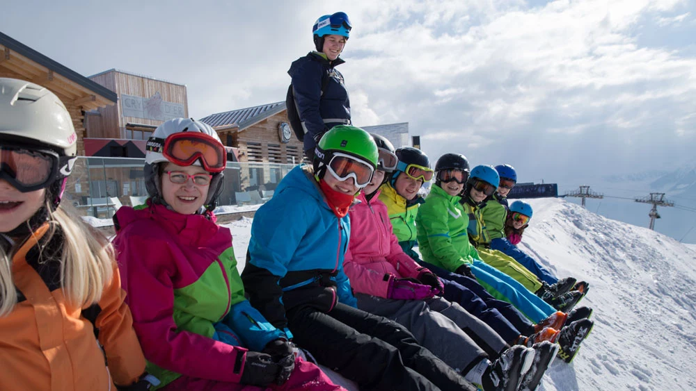 Kinder sitzen als Gruppe vor einer Skihütte
